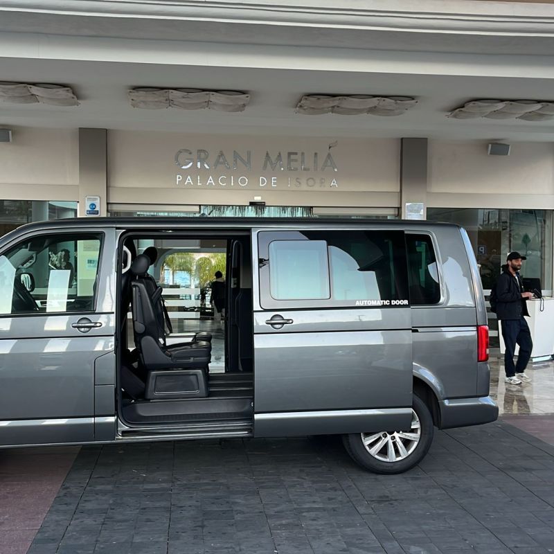 Gray van parked in front of hotel entrance, with open sliding door and luggage nearby.